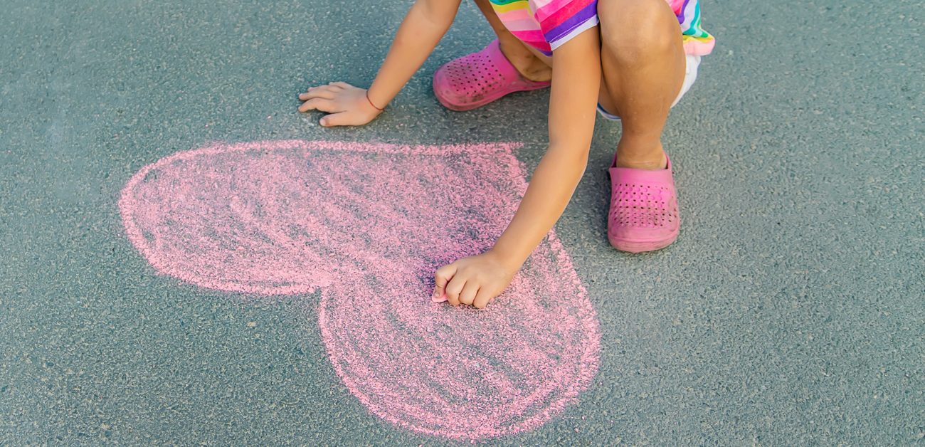 child drawing heart with chalk on sidewalk