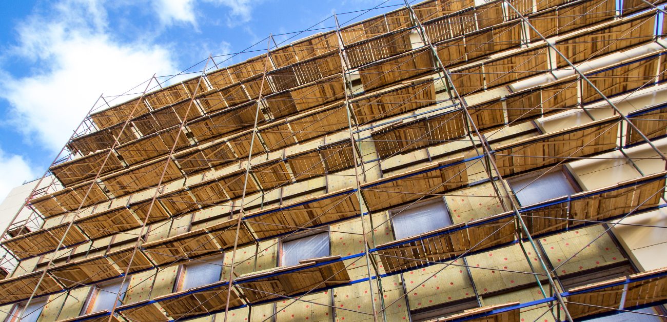A picture of a scaffolding along a side of a building, leading up to the roof with sky in the background