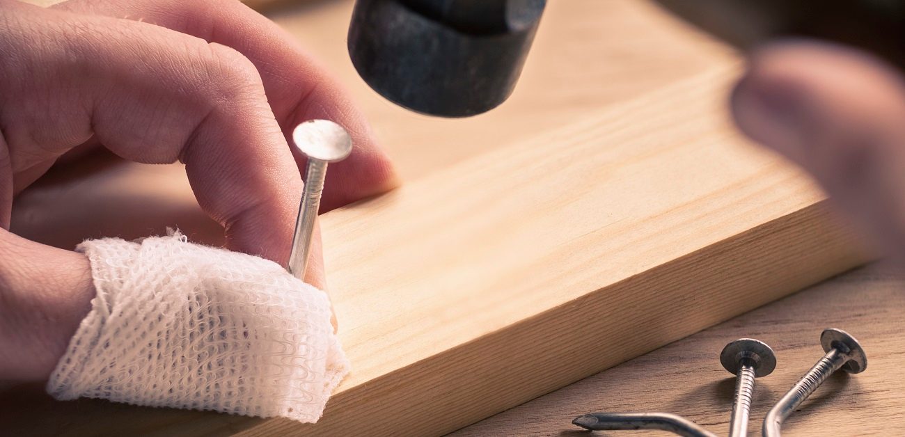 Bandaged finger holding nail on wood