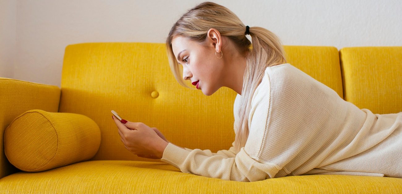 woman lying on sofa, using smartphone