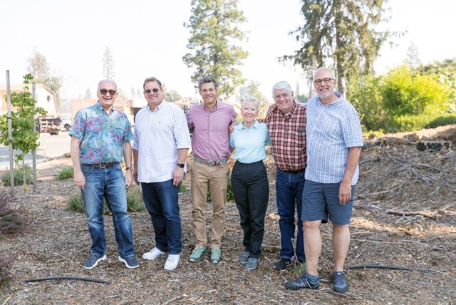A picture of six people on a rebuilding team from CRE on a visit to Paradise, Calif., standing near trees and bushes near homes.