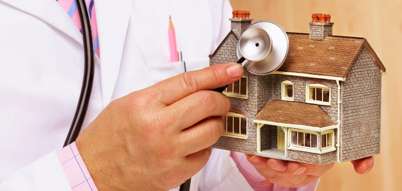 Doctor holding stethoscope to model house.