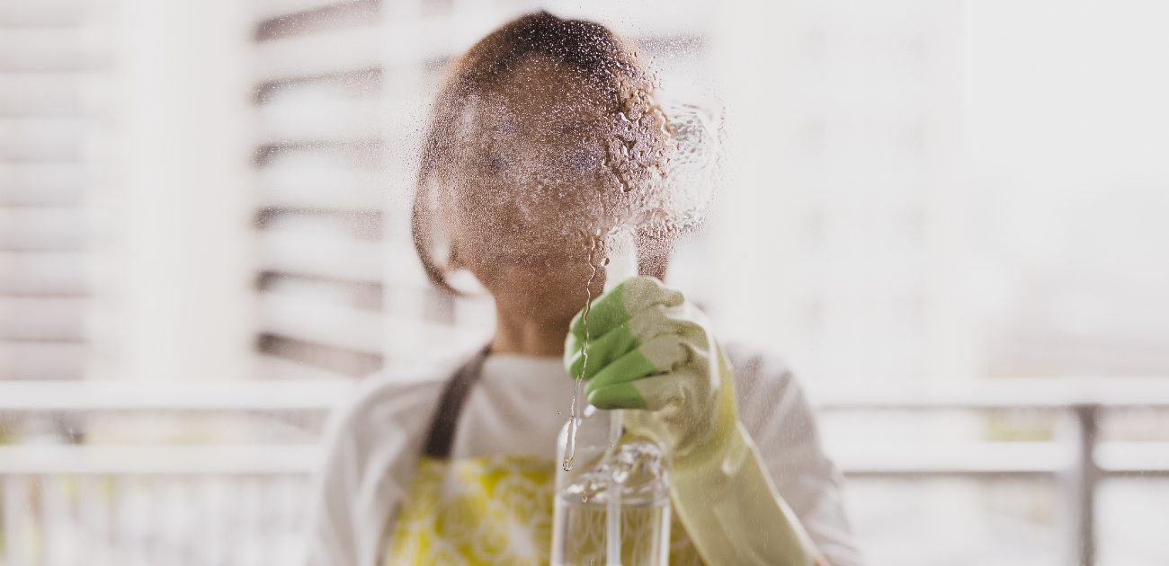 A picture of a woman spraying cleaner on a glass wall, distorting the view of her face.