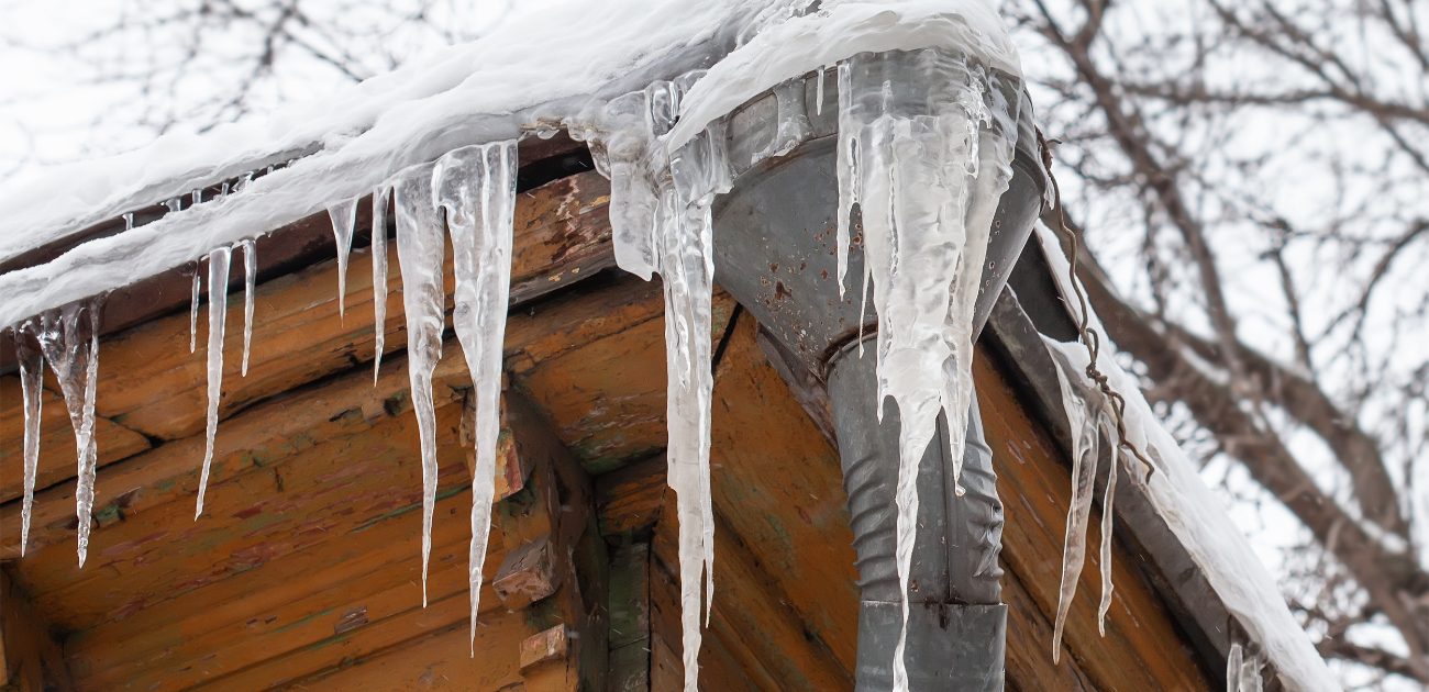 A picture of a home's exterior gutter, with icicles forming down along it and snow on top.