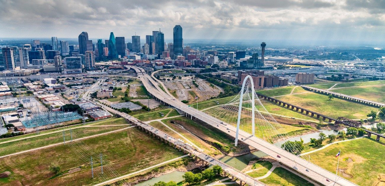 An aerial photograph of a city's downtown from a distance, showing a bridge over fields and roads leading into the metro area.