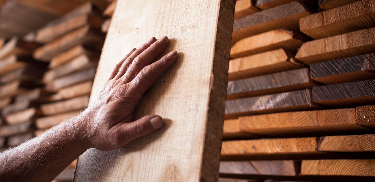 A person's hand rests on a piece of lumber standing vertically against the wall.