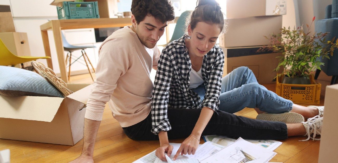 A man and a woman couple sit together on the floor going over remodeling plans.