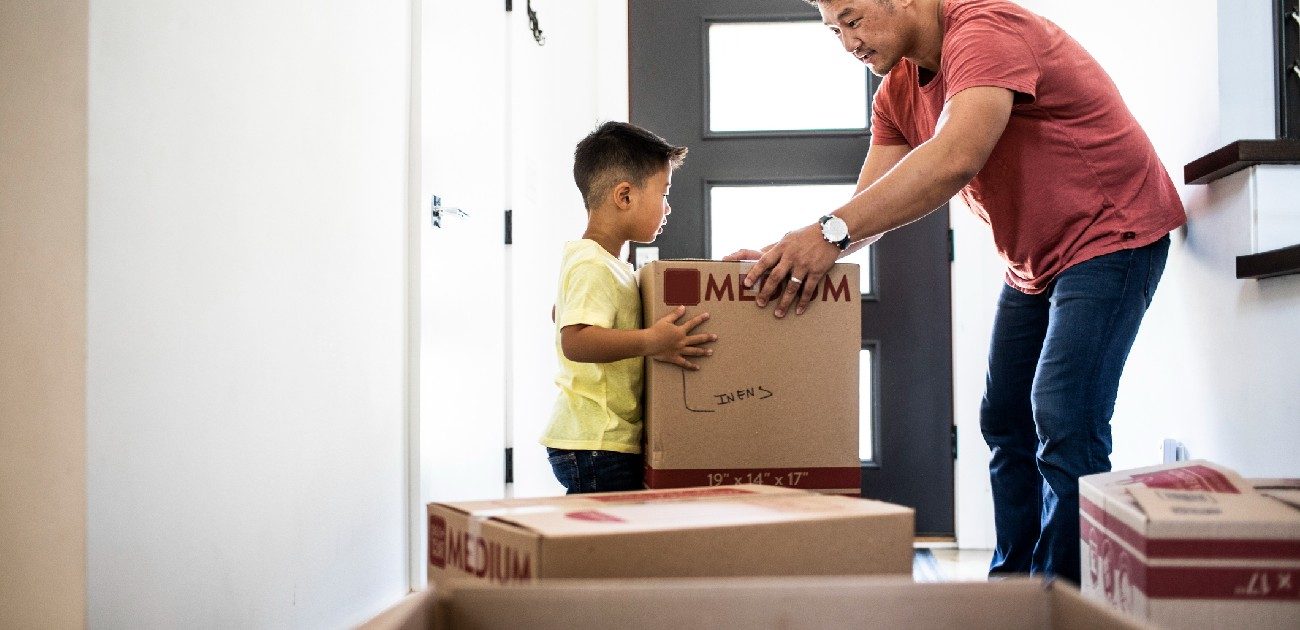 A father hands his young son a moving box inside a home.