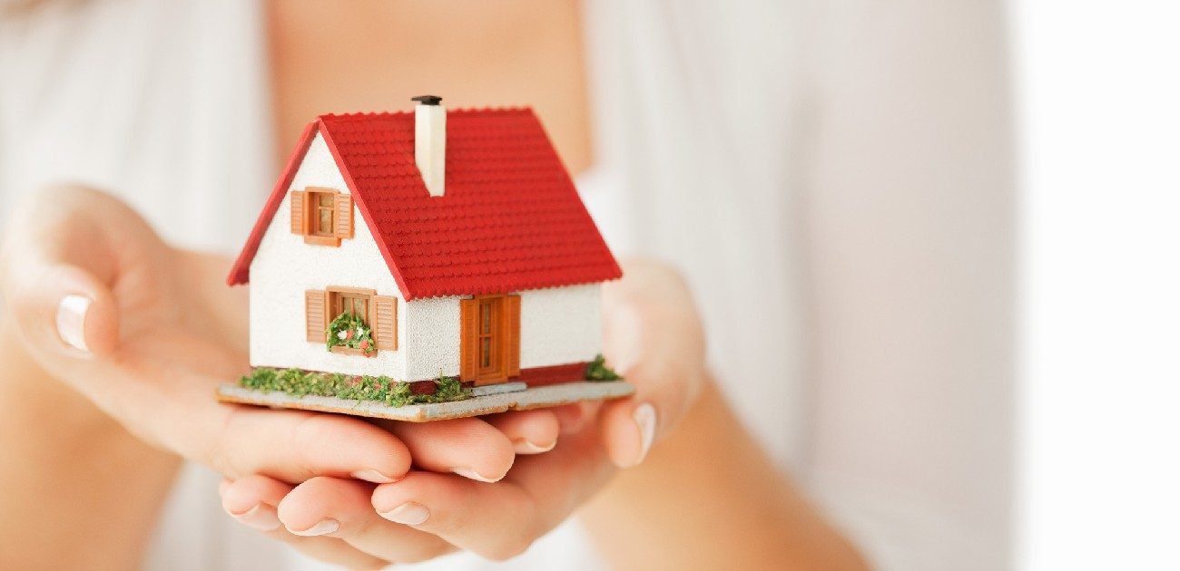 Picture of a person holding a house miniature.