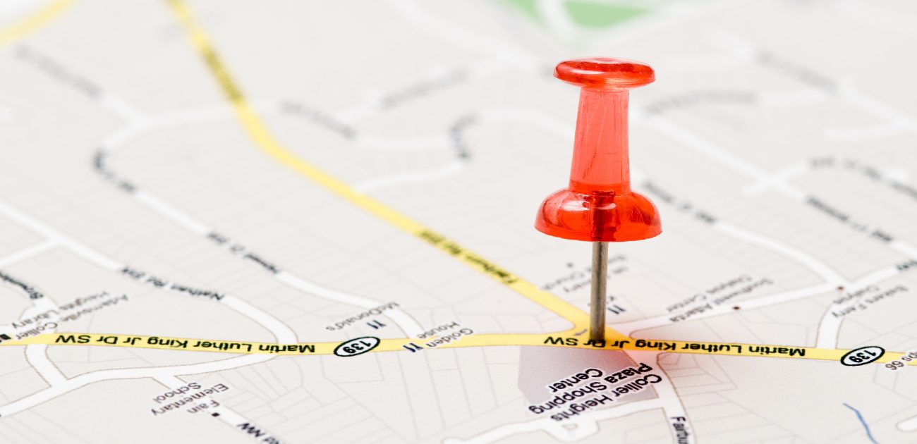 An image of a red pushpin stuck into a printed Google map.