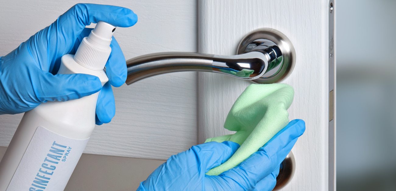 person cleaning doorknob with disinfectant