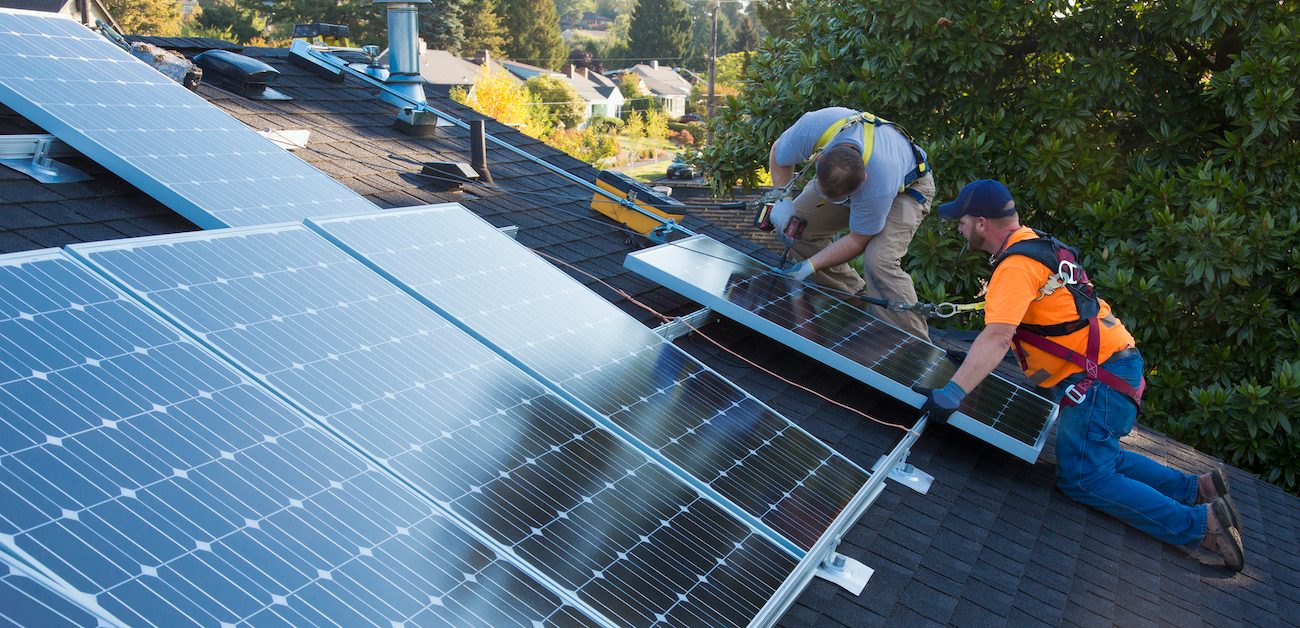 Two men installing solar panels on house roof.
