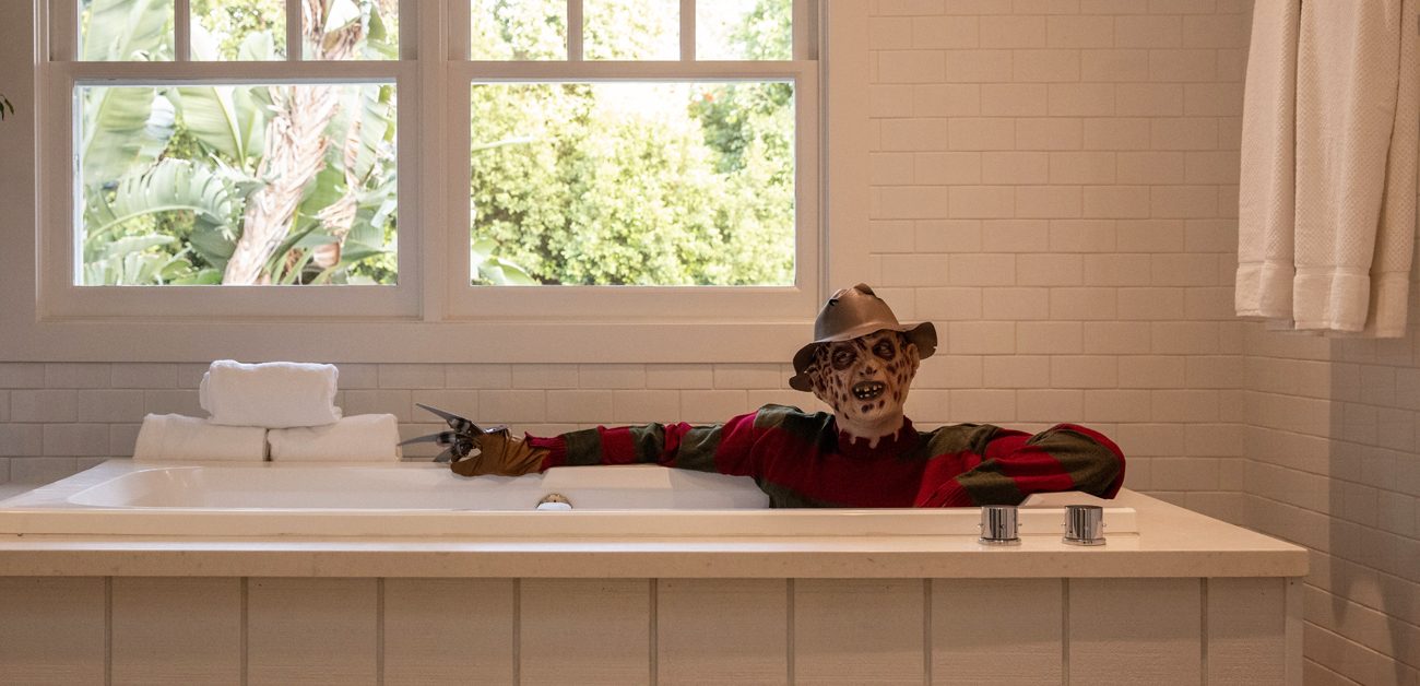 A costumed Freddy Krueger posing in the bathtub of the famous horror flick's house.