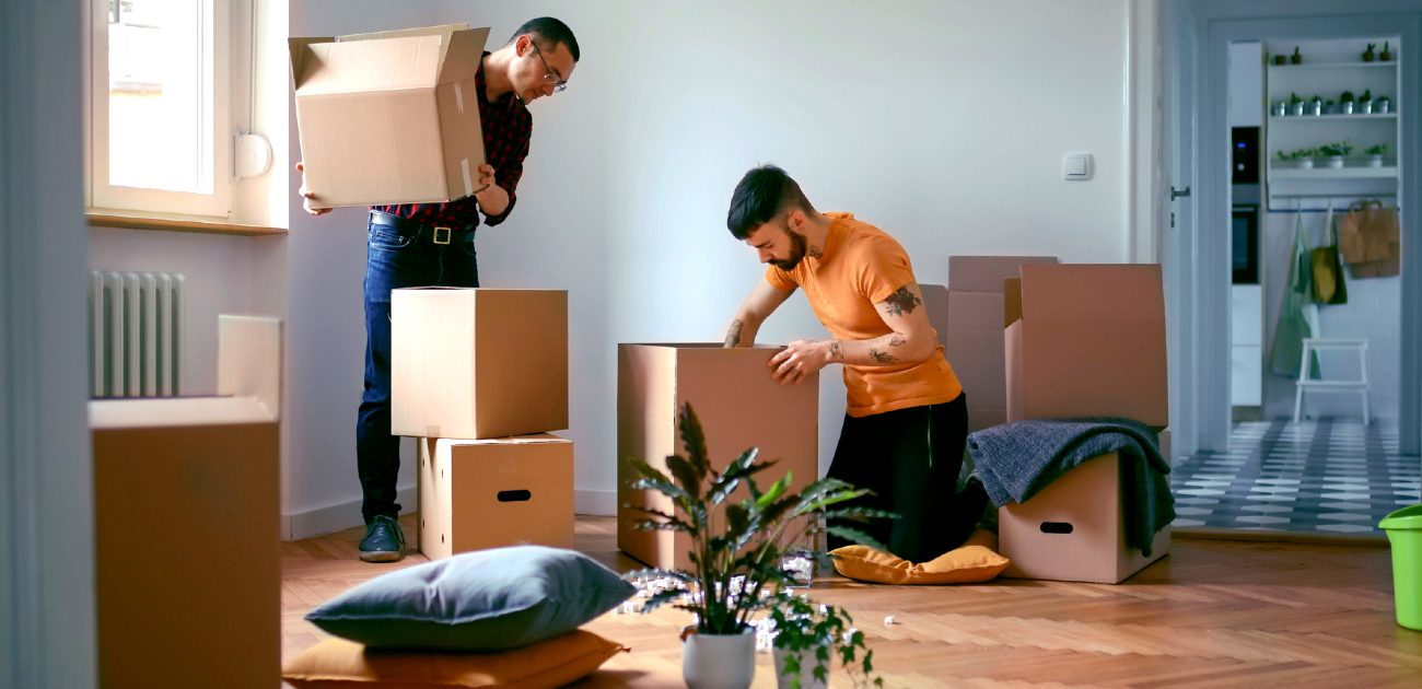 Two men carry and unpack boxes in a new home.