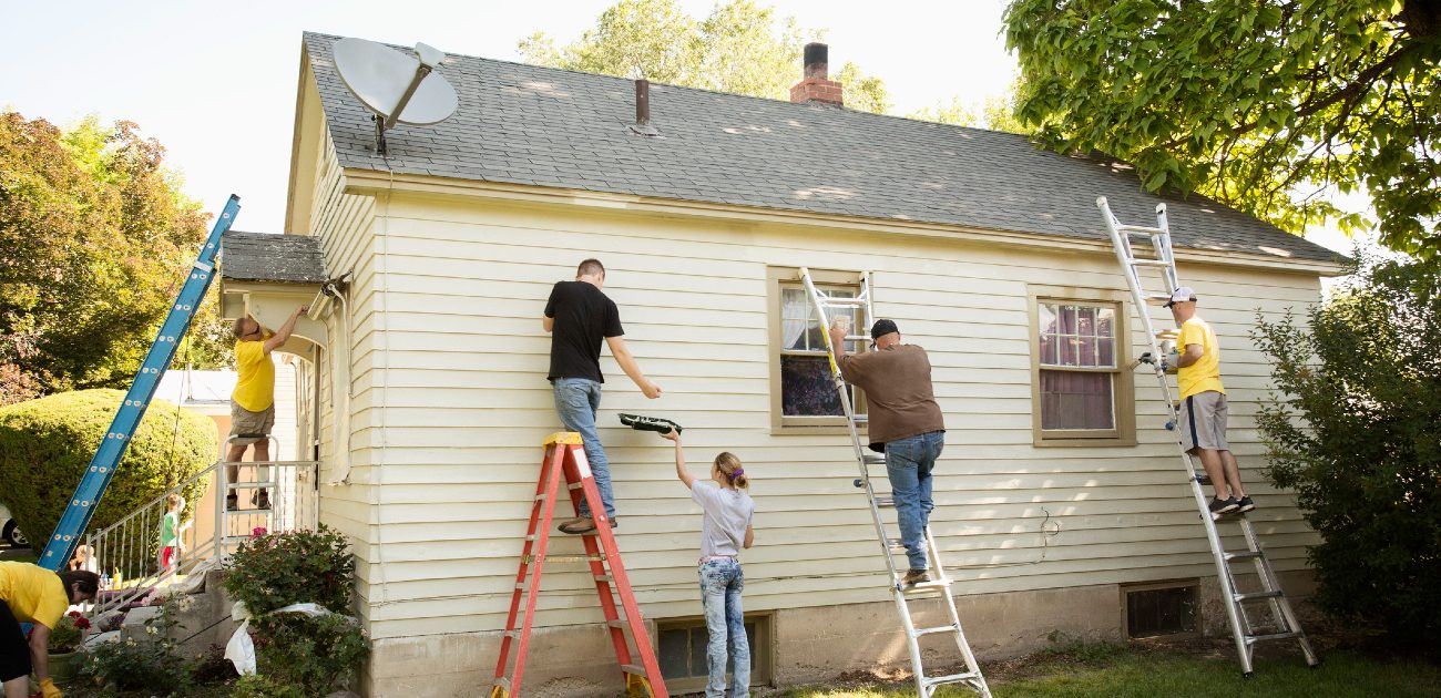 A group of people on ladders paint the side of a house