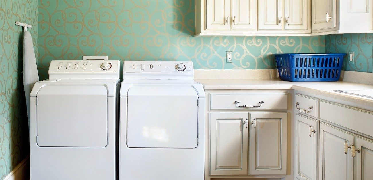 A picture of a laundry room with a washer, dryer, and set of cupboards next to them.