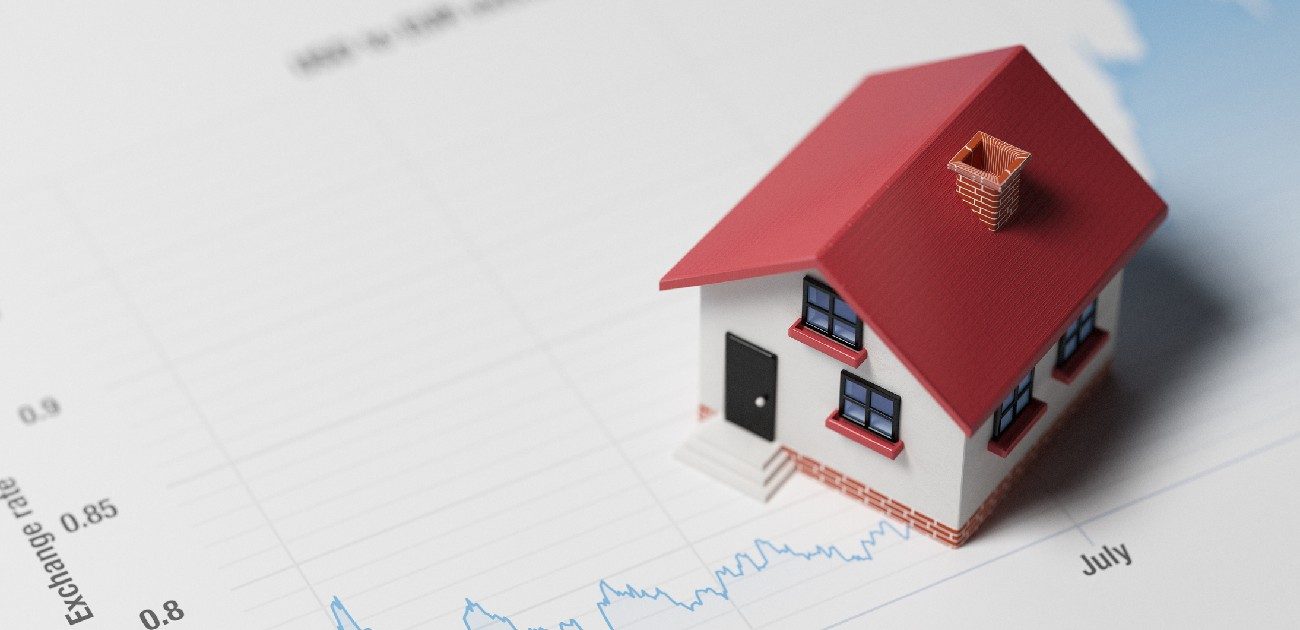 A picture of a house miniature sitting on a printed line graph charing housing prices.