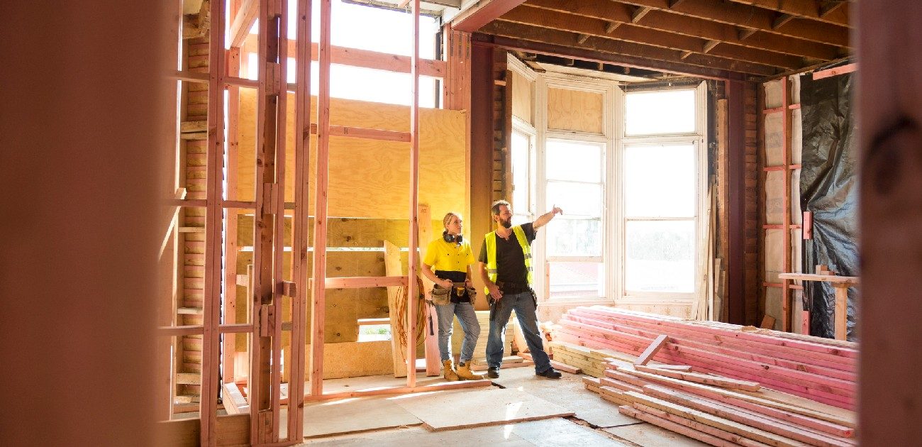 Two construction workers stand in the interior of a home being built.