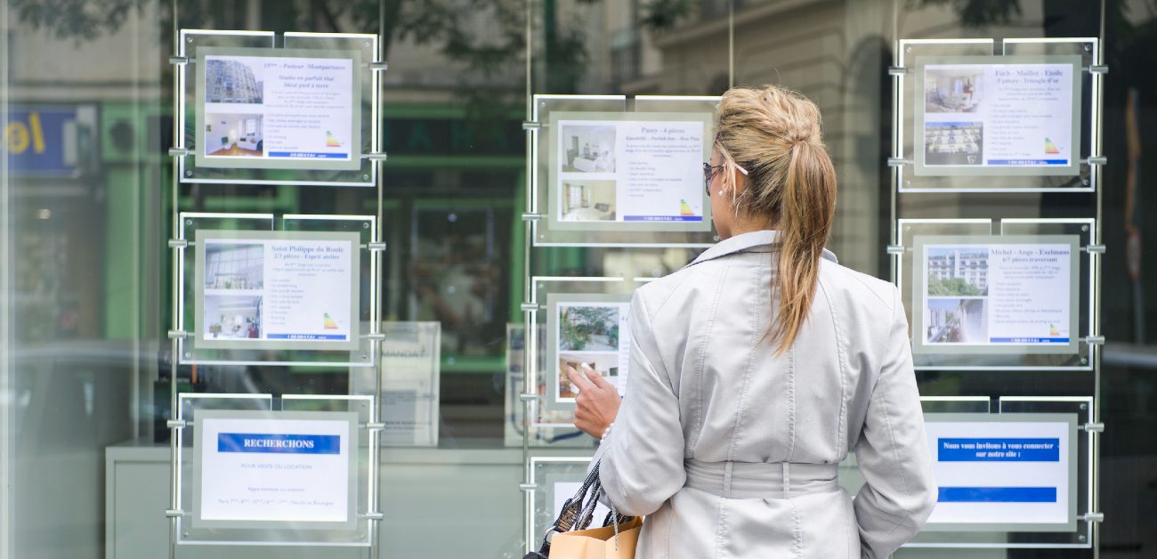 A picture of a woman facing away from the camera at a glass wall displaying listings and housing information.
