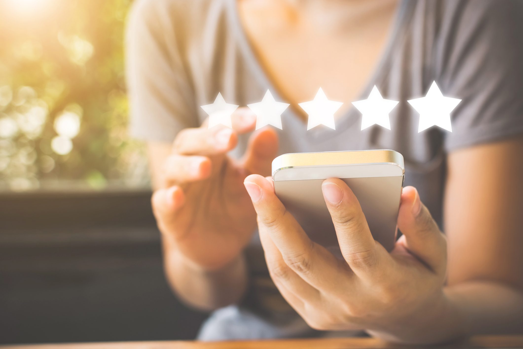 A person in a gray shirt holding a phone with five white stars above the phone