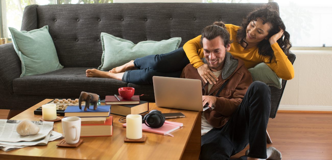 A man and a woman relax on their living room sofa while the man uses a laptop on the coffee table.