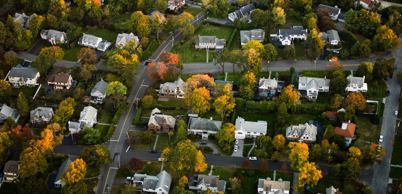 An overhead shot of a suburban residential neighborhood with houses and roads among scattered trees.