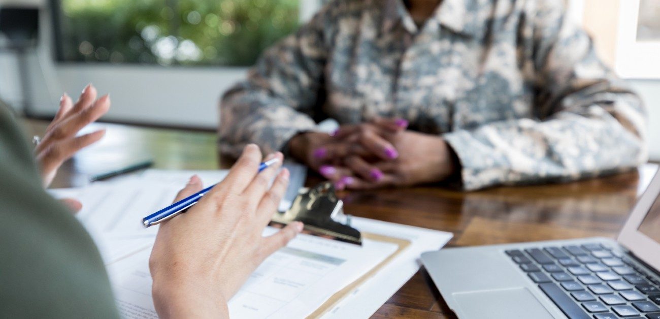 A member of the U.S. military sits at a desk applying for a VA loan with the lender sitting across from them.