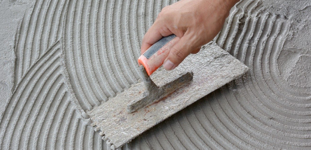 A picture of someone using a notched trowel to smooth out cement.