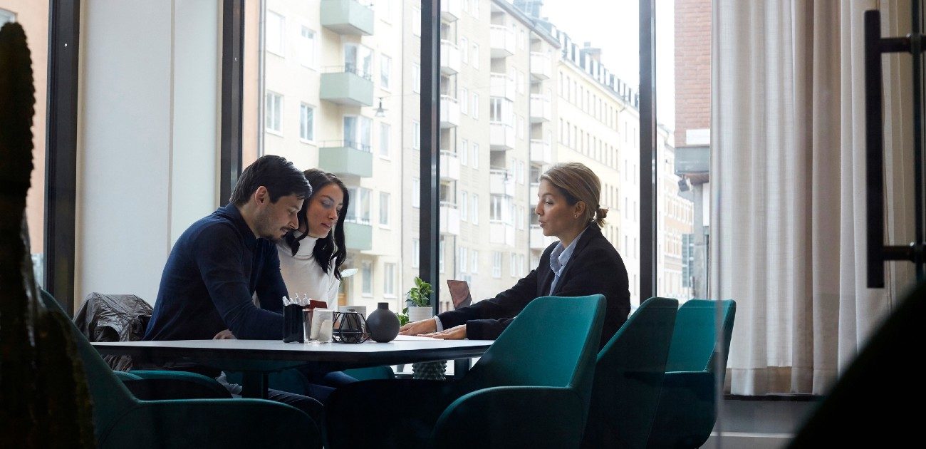 A group of three people sits at a table in a cafe with large windows behind them.