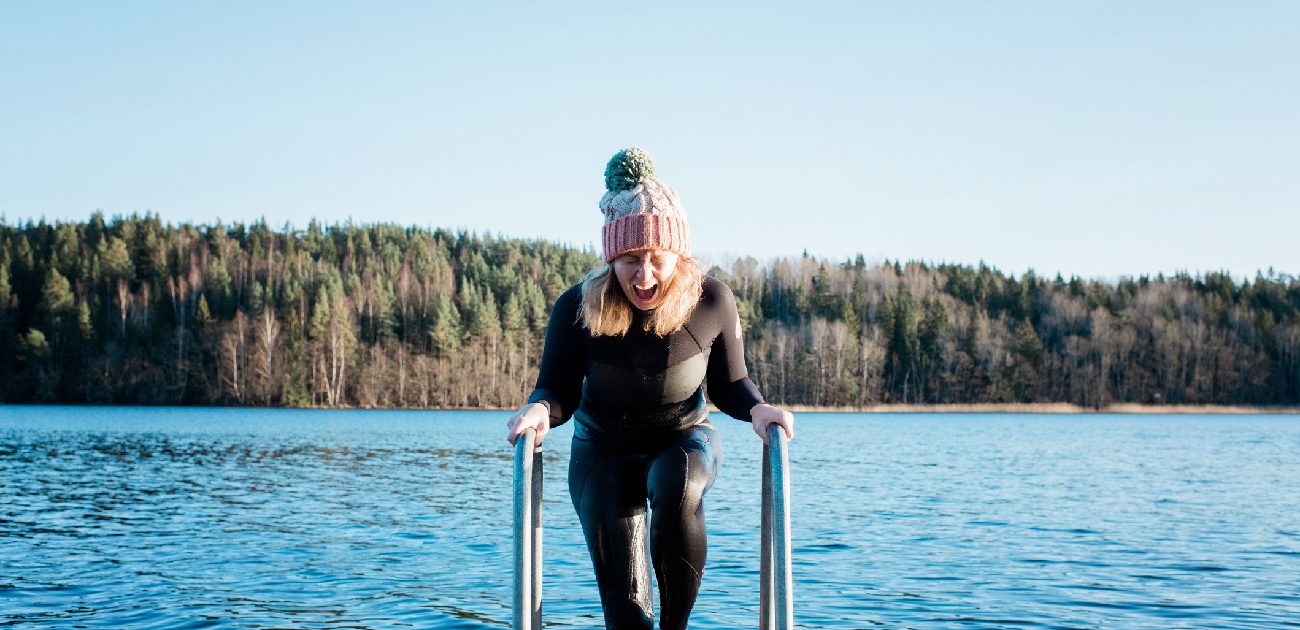 A woman in a body suit climbs out of a cold lake on a ladder onto a dock.