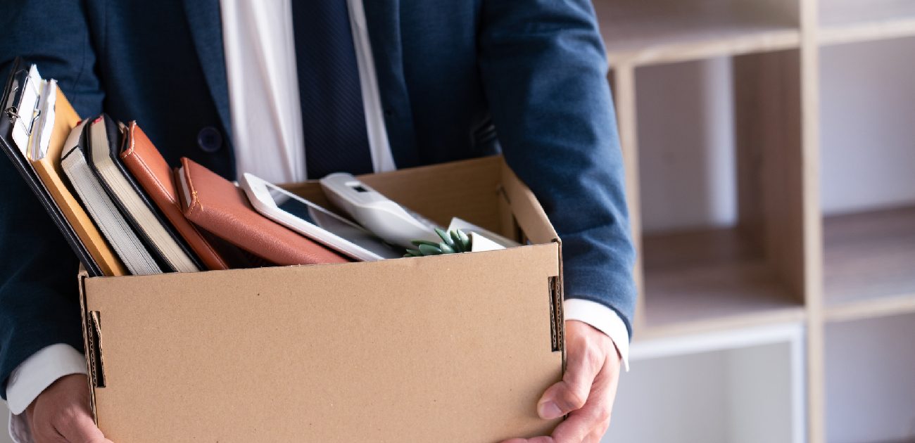 A picture of a man in a suit holding a box filled with books and office supplies.