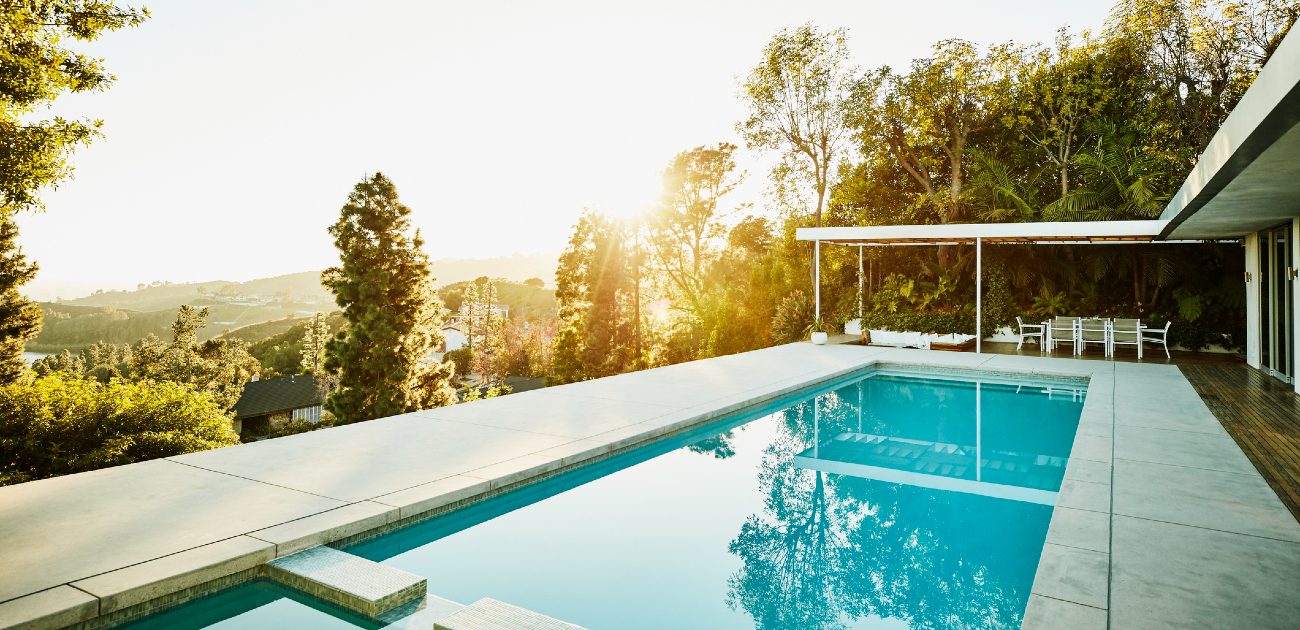 A picture of a home's backyard pool, with the view of trees and distant, low hills toward the horizon.