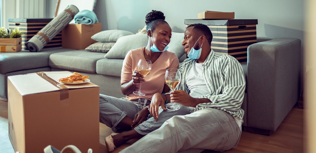 A man and a woman eat a meal and have a glass of wine using a moving box for a table in a new home.