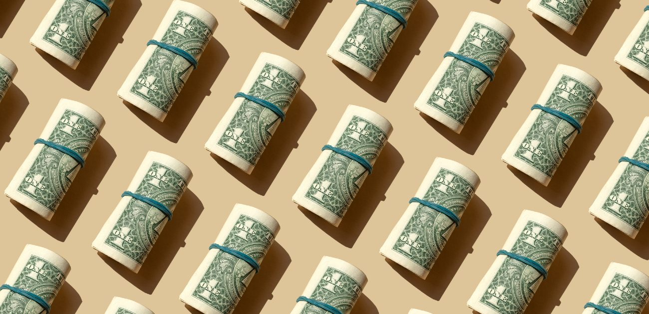 A picture of single dollar bills rolled up in blue rubber bands arranged repeatedly across the image.