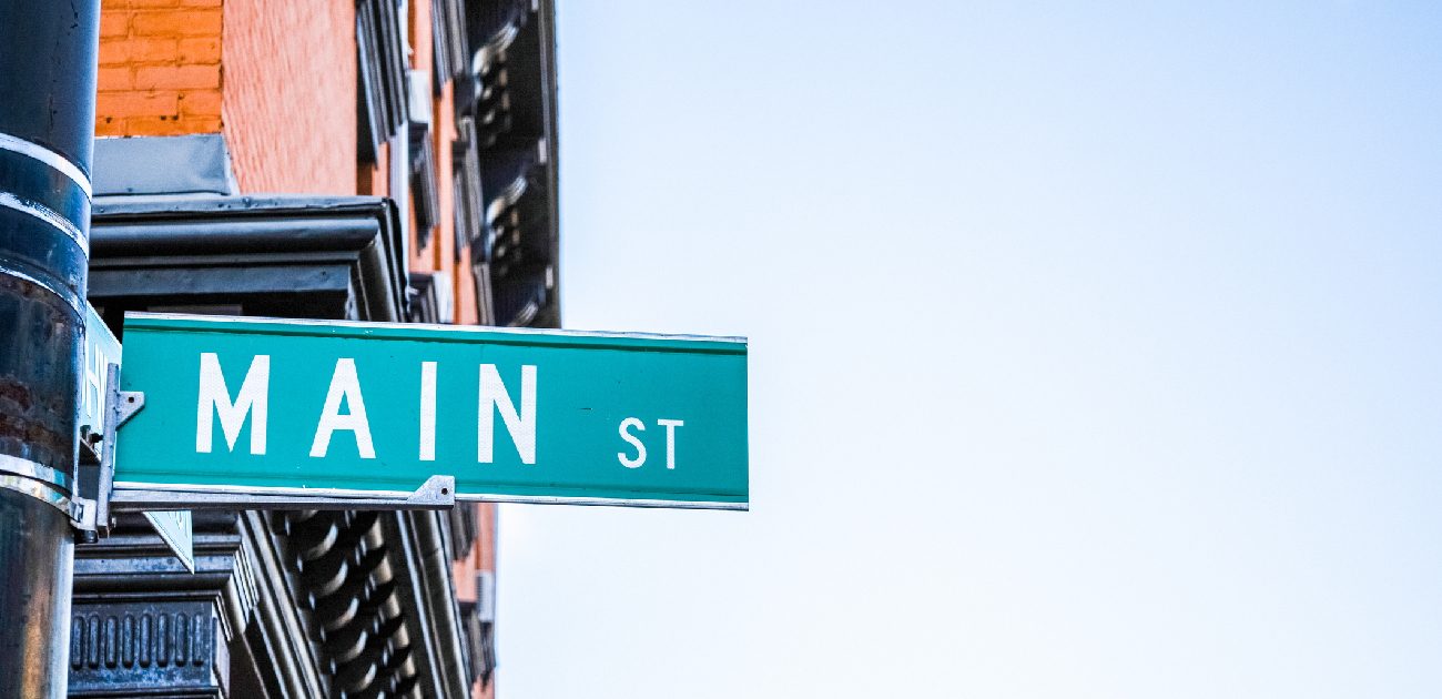 A picture of a street name sign that reads "MAIN ST" with the upper part of a building behind it.