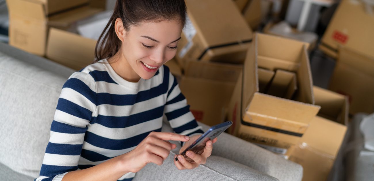 woman texting on cell phone, surrounded by moving boxes