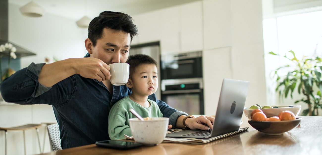 Father multitasking at computer with child in lap.