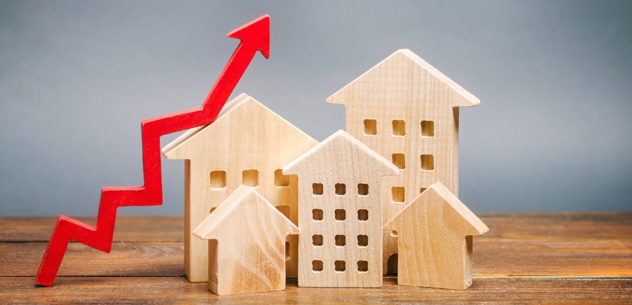 A picture of five wooden house miniatures next to a wooden, jagged-shaped red arrow mimicking rate increases on a graph.