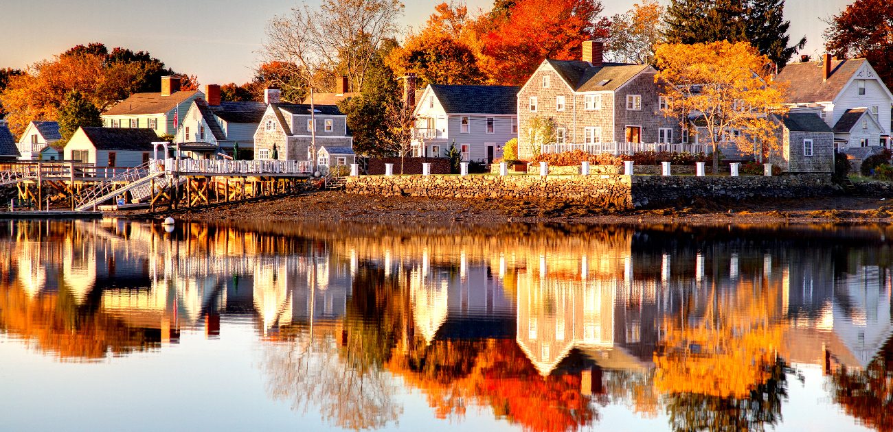 A picture of lakeside homes in autumn, with the water reflecting the houses in view.