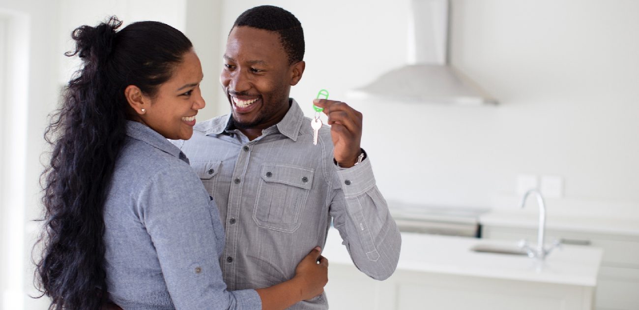 A Black man and woman hugging and smiling, while the man holds keys to their new home.
