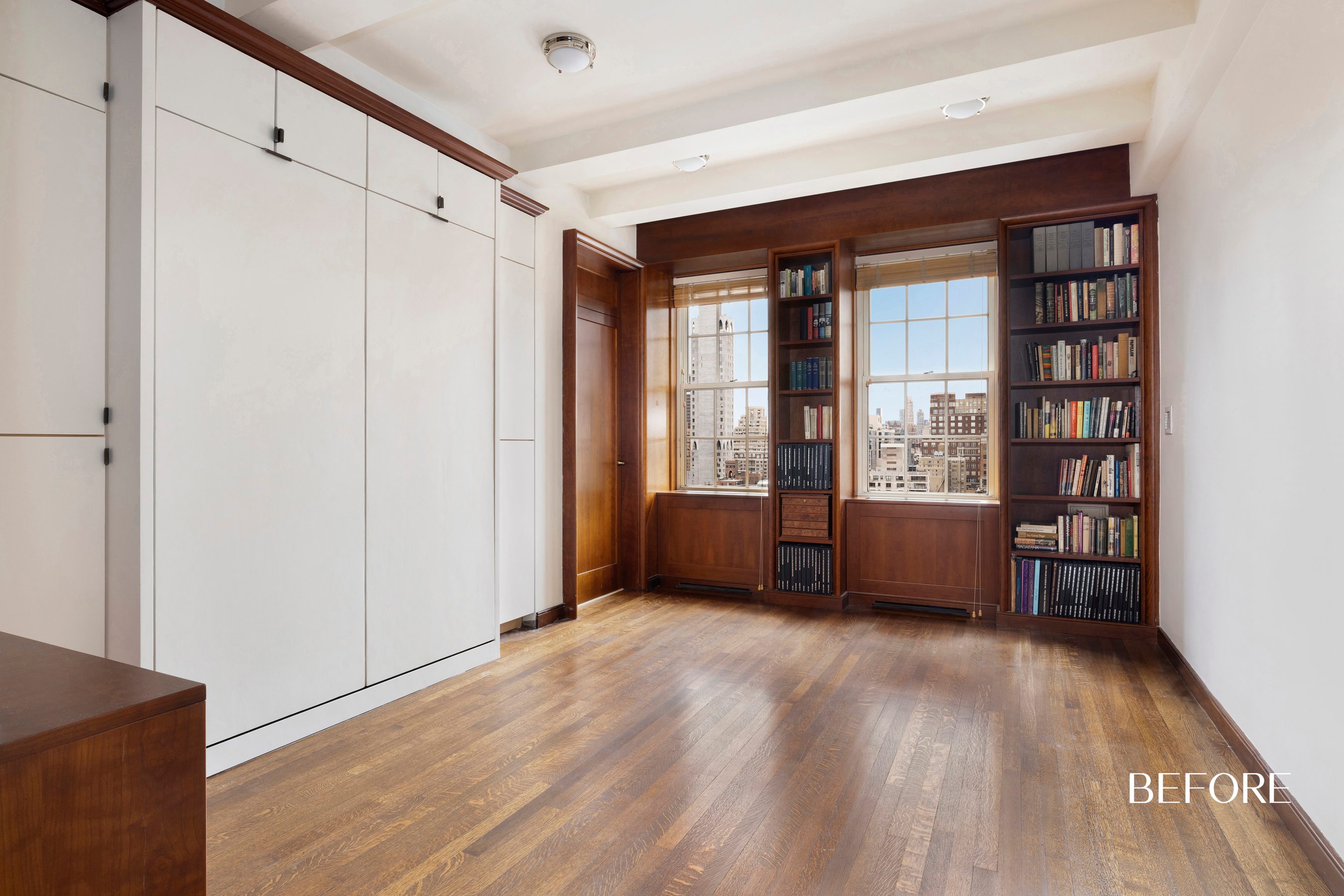 An empty room with windows and brown built-in bookshelves flanking the windows