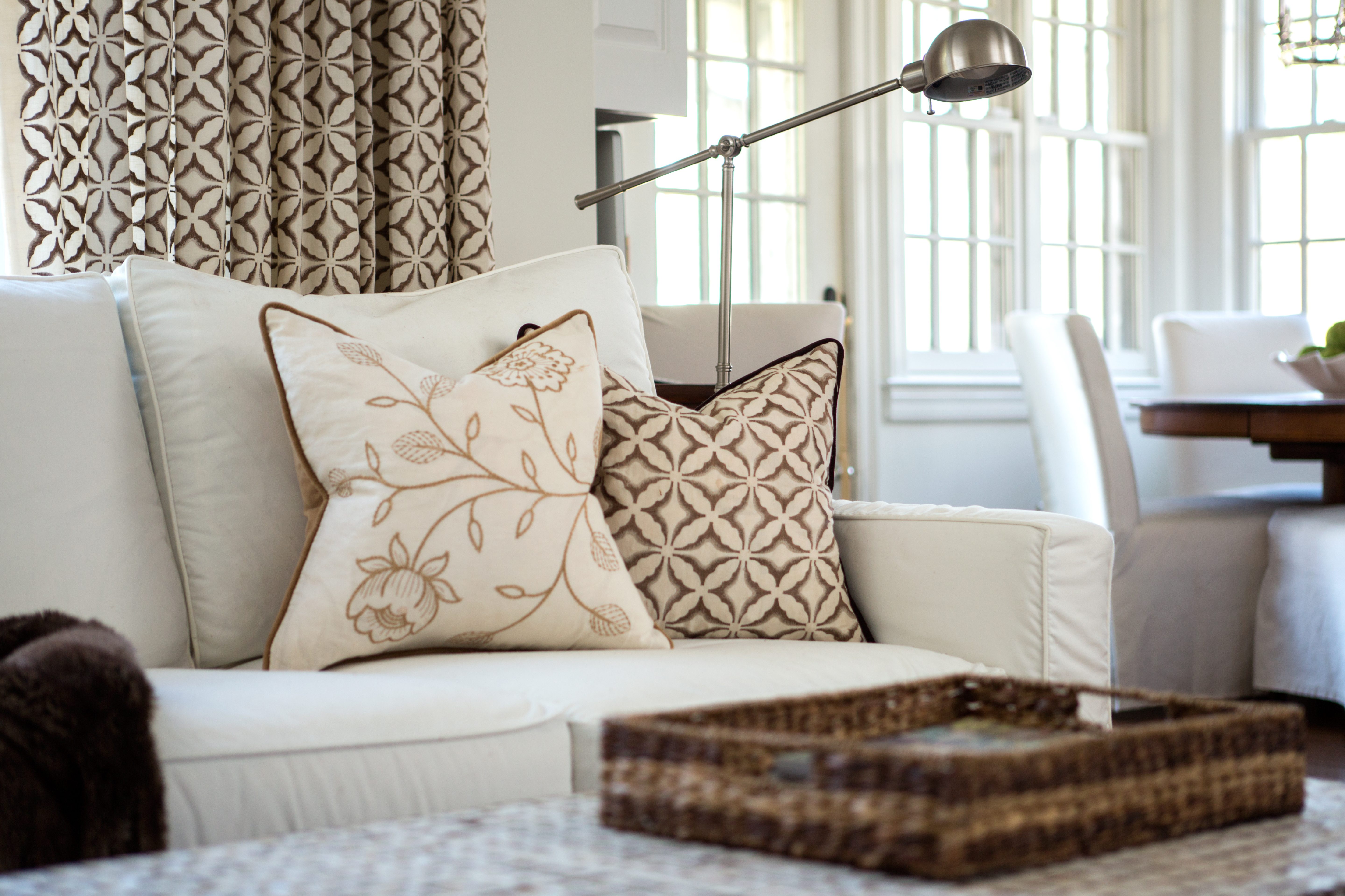 Close-up photo of a couch with warm-toned pillows and matching window treatments behind